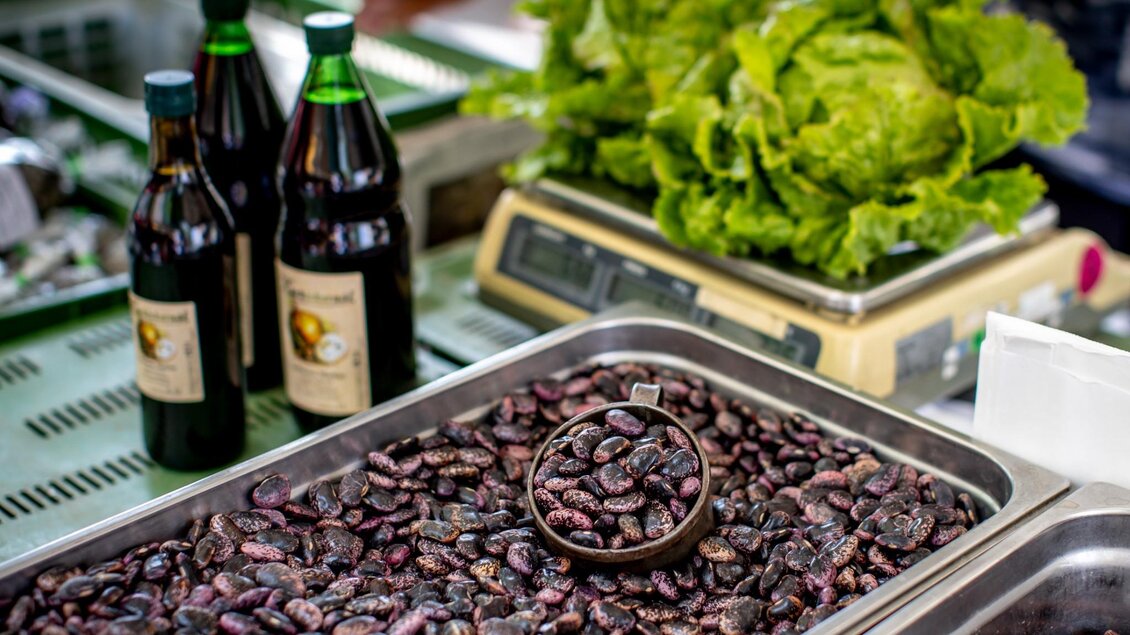 Edelkäferbohnen in einer Metallschale am Marktstand, daneben Flaschen Öl und frischer grüner Salat | © Graz Tourismus - Tom Lamm