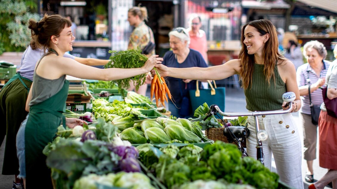 Frau mit Fahrrad kauft Bund Karotten an einem Gemüse-Stand am Kaiser-Josef-Markt in Graz | © Graz Tourismus - Tom Lamm