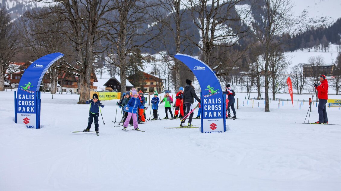 Ein Wintersportort mit Kindern, die Skilanglauf im Kalis Cross Park lernen. Im Hintergrund sind schneebedeckte Berge und Bäume zu sehen. | © Loretta Kvitek