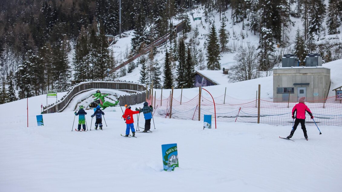 Eine Gruppe von Skifahrern gelangt auf eine schneebedeckte Piste. Im Hintergrund sind Bäume und ein Übungshang sichtbar. | © Loretta Kvitek