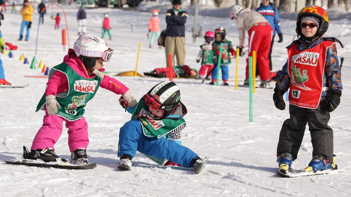 Eine Gruppe von Kindern lernt Skifahren auf einer verschneiten Piste. Zwei Kinder spielen zusammen, während ein weiteres Kind beobachtet. | © Hans-Peter Steiner