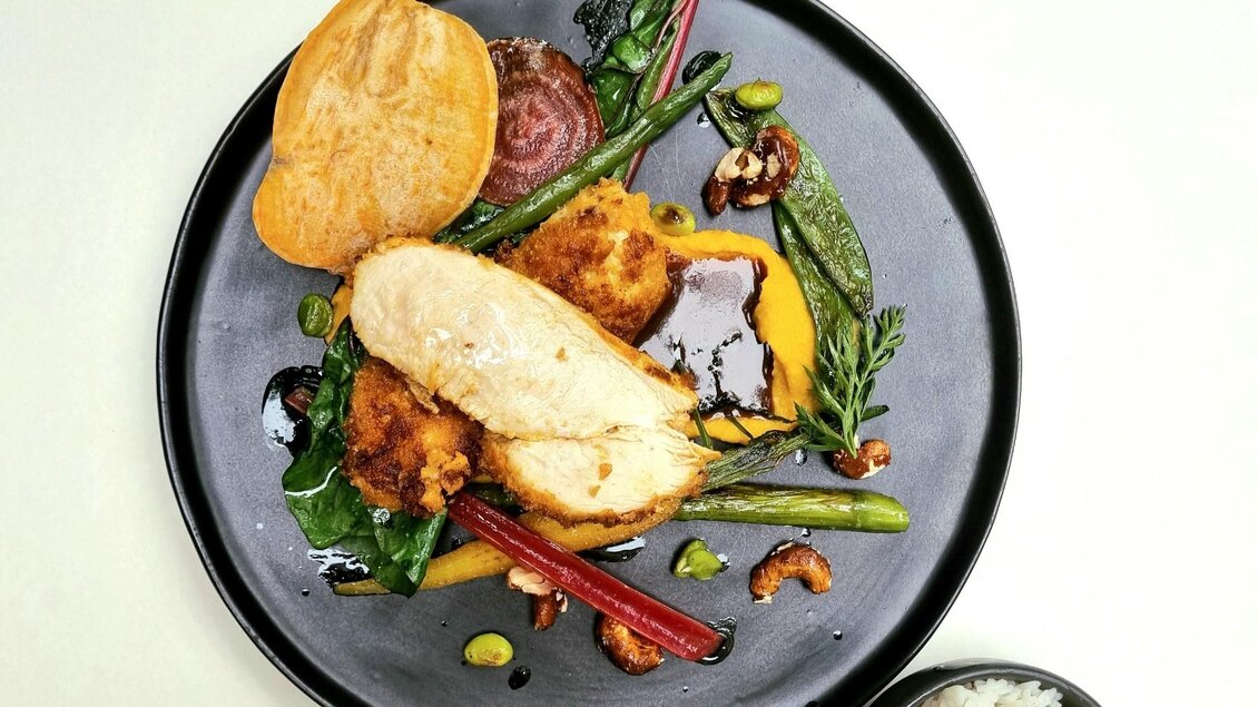 Ein schön angerichteter Teller mit gebratenem Hähnchen, buntem Gemüse und verschiedenen Nüssen. Neben dem Hauptgericht befindet sich eine Schale mit Reis. | © Kalte Ente