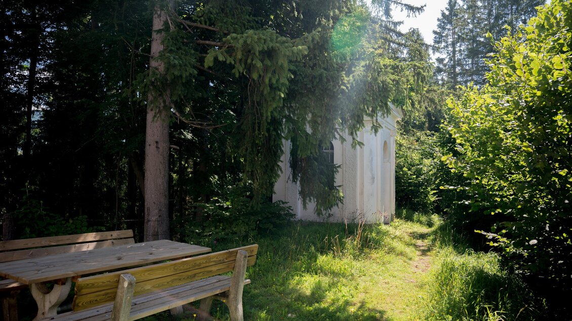 Eine kleine, weiße Hütte steht zwischen hohen Bäumen. Ein Holztisch lädt zum Entspannen in der Natur ein. | © Anita Fössl