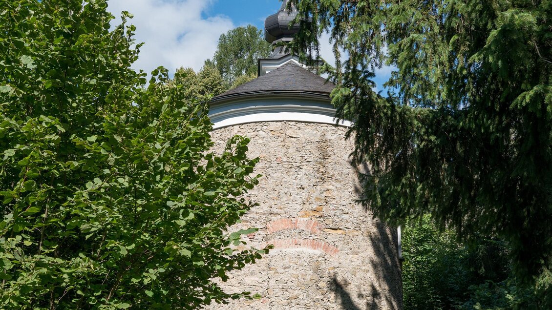 Ein historischer Turm, umgeben von Bäumen und Grün. Der Himmel ist klar mit ein paar Wolken. | © Anita Fössl