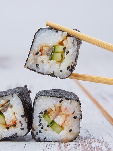 Three pieces of sushi with rice, cucumber, and fish, wrapped in nori, one of which is being held with chopsticks. | © Pixabay