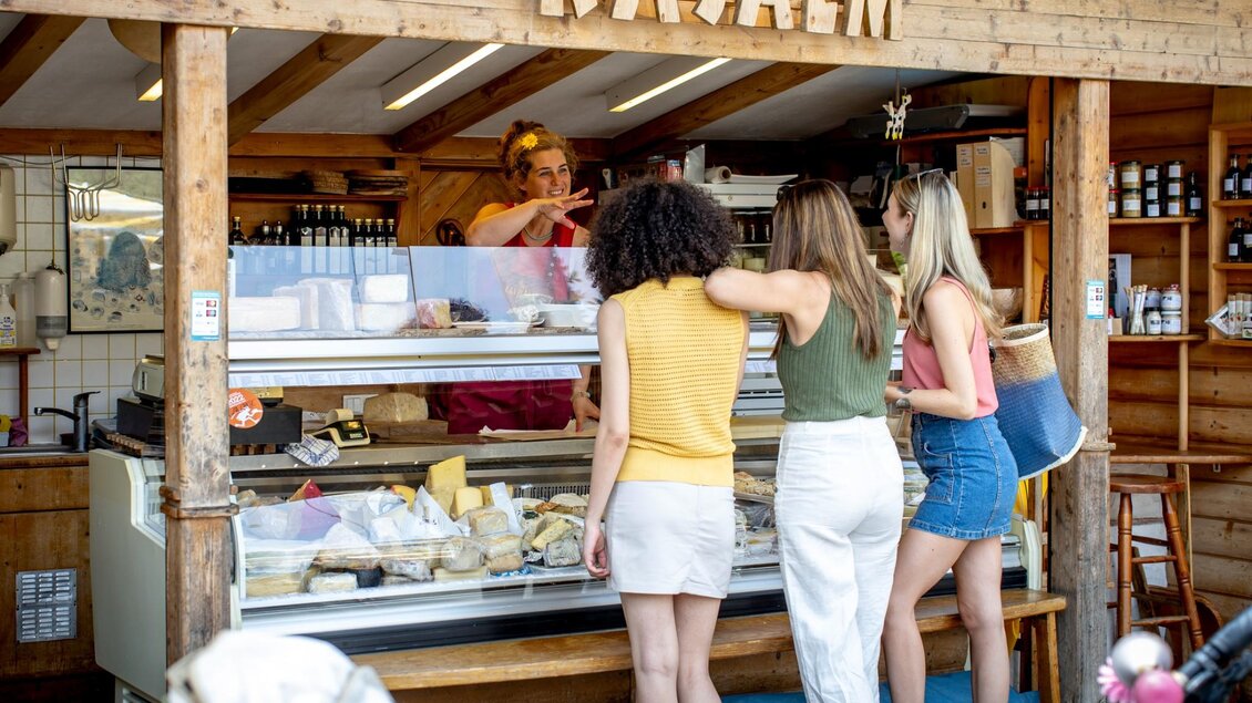 Drei Frauen stehen vor einer Käsetheke und unterhalten sich mit der Verkäuferin, im Vordergrund ein Fahrradlenker | © Graz Tourismus - Tom Lamm