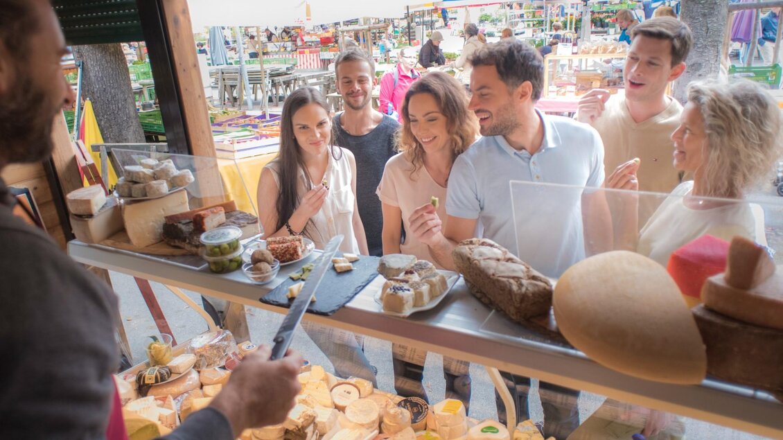 Gruppe von Menschen probiert verschiedene Käse- und Brotsorten an einer Theke mit regionalen Produkten | © Graz Tourismus - Gerald Plattner