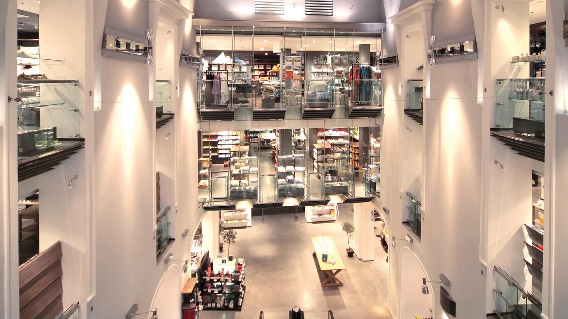 Lichtdurchfluteter Innenraum eines mehrstöckigen Kaufhauses mit Rolltreppen und Warenpräsentation | © Kastner & Öhler