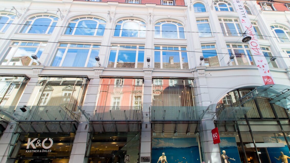 Passant:innen vor einer Altbaufassade mit großen Schaufenstern und moderner Glasüberdachung in Graz | © Graz Tourismus - Harry Schiffer