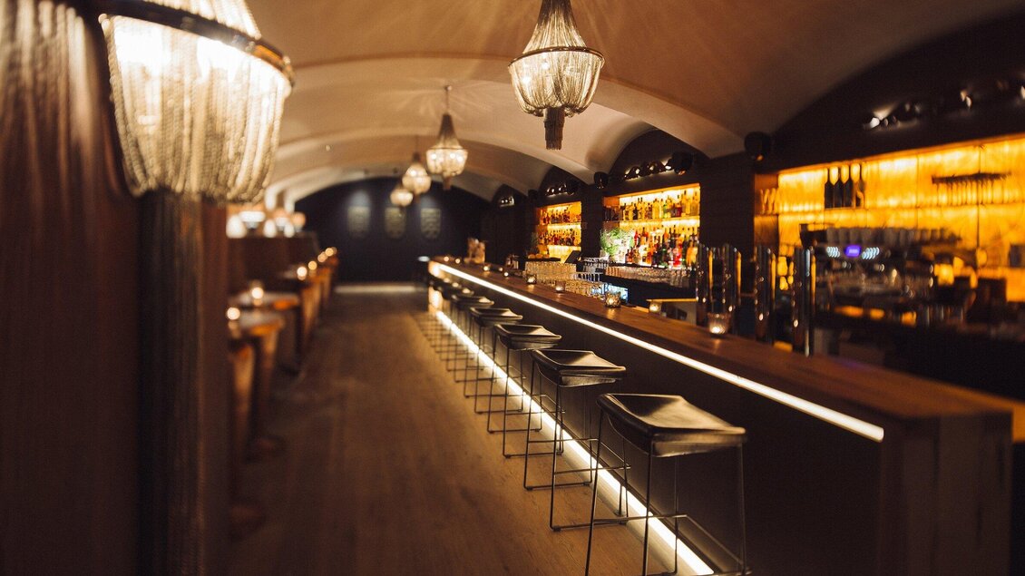 Eine elegante Bar mit stilvollen Leuchtern und warmem Licht. Die langen Barhocker laden zum Verweilen ein. | © Katze Katze