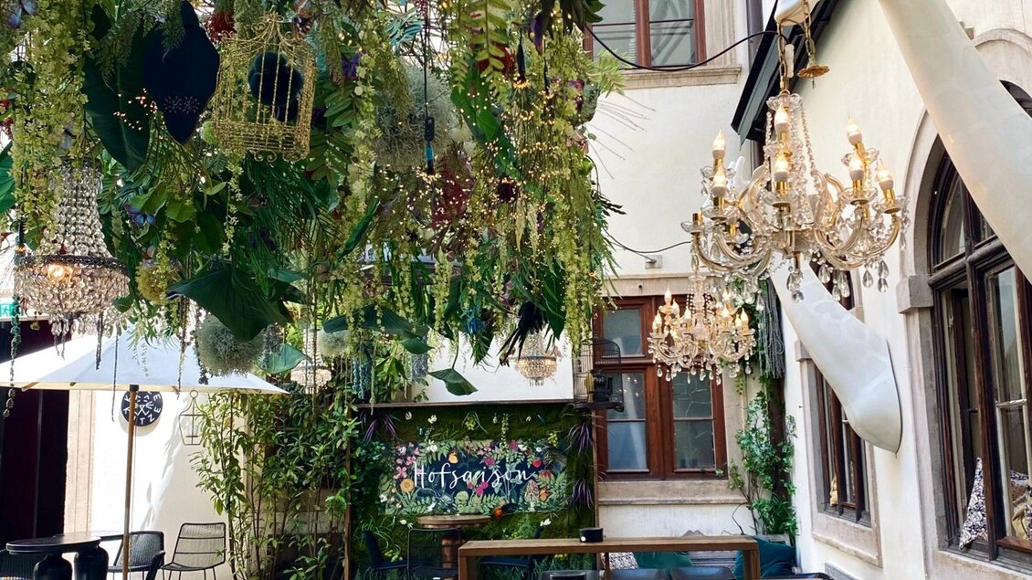 Ein charmantes Café mit üppigen Pflanzen und eleganten Kronleuchtern. Der Innenhof bietet eine einladende Atmosphäre zum Entspannen. | © Katze Katze