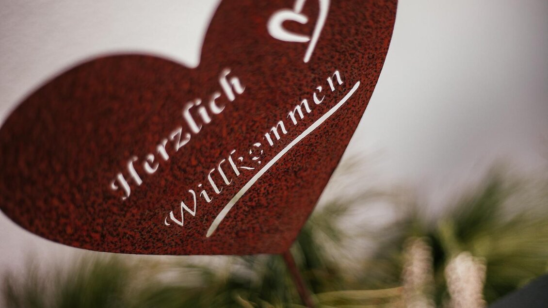 Ein herzförmiges Schild mit der Aufschrift "Herzlich Willkommen". Das Schild ist dekorativ und lädt freundlich ein. | © Damira Slodnjak