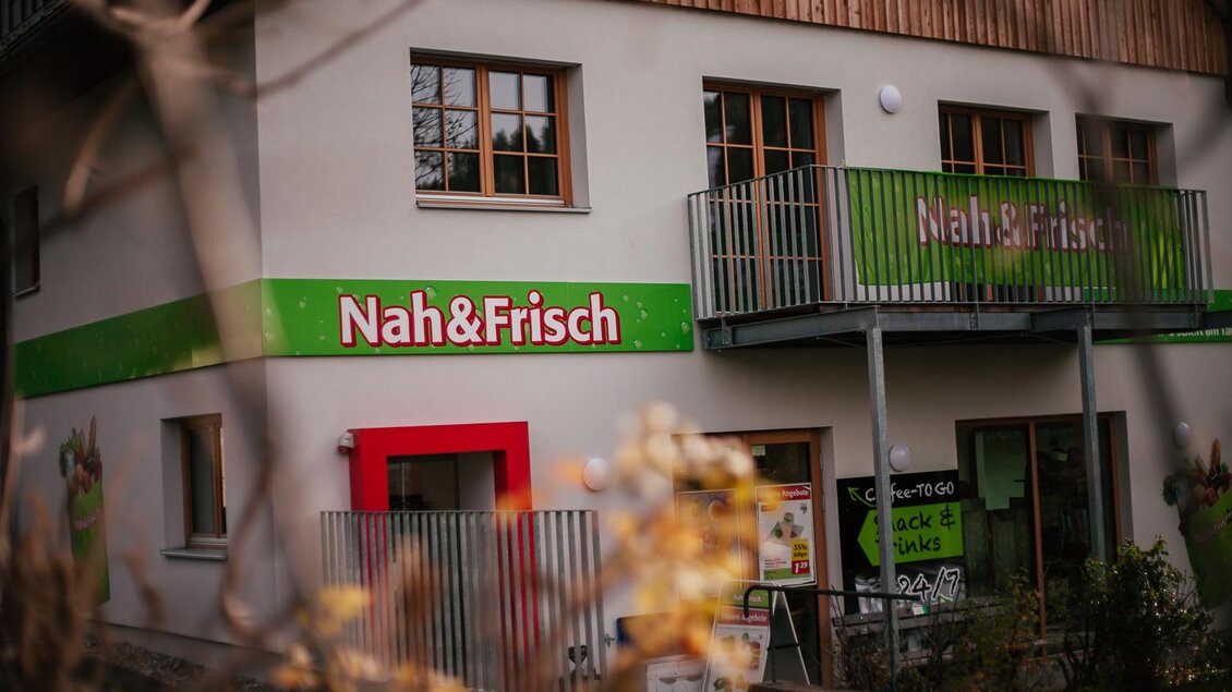 Ein Geschäft namens "Nah&Frisch" mit zwei Stockwerken und einem Balkon. Die Fassade ist hell und freundlich gestaltet, mit großen Fenstern und einem einladenden Eingang. | © Damira Slodnjak