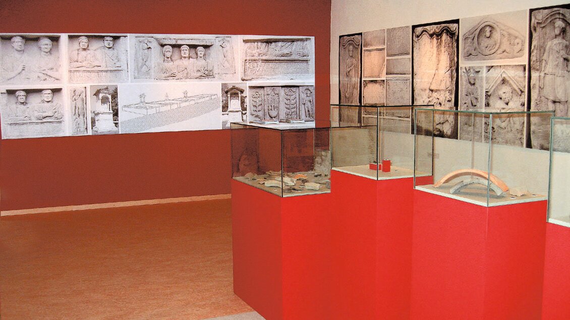 Ein Museum mit rot gestrichenen Wänden, in dem Vitrinen mit historischen Artefakten stehen. An der Wand sind große Fotografien von Reliefs und Statuen zu sehen. | © Gemeinde Geistthal-Södingberg