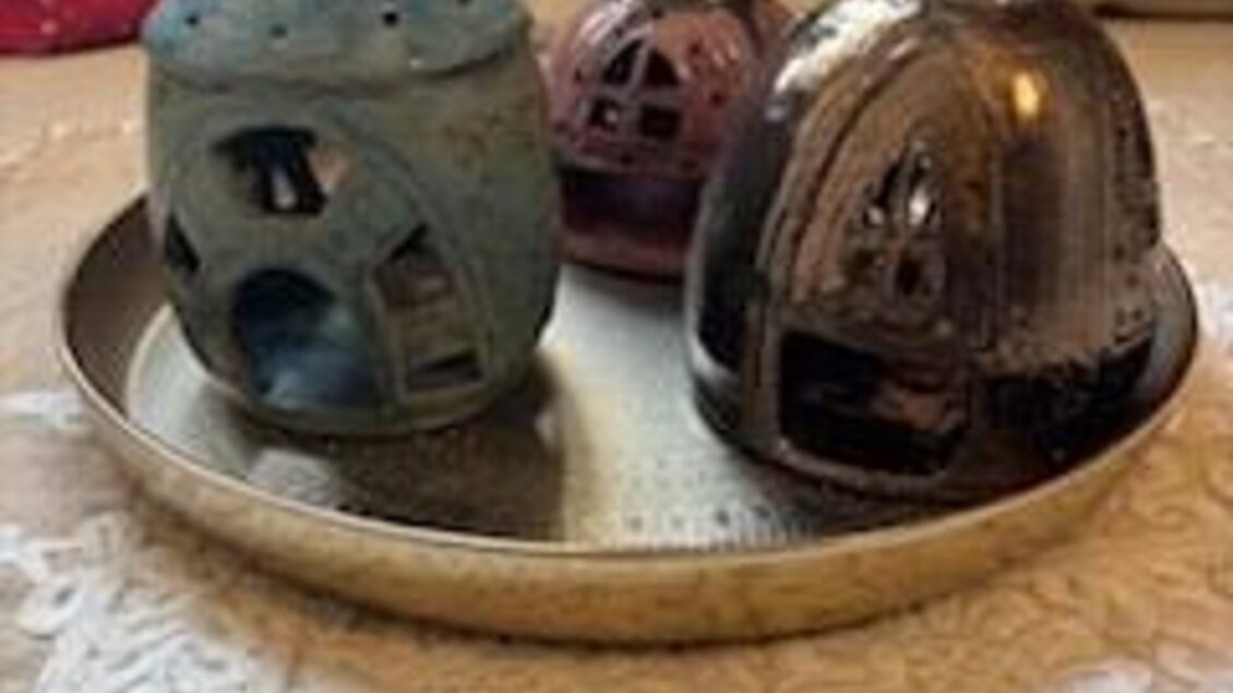 Drei keramische Gebäude in verschiedenen Farben auf einem silbernen Tablett. Der Hintergrund zeigt eine gemütliche Textilumgebung. | © Keramik Werkstatt Uhring