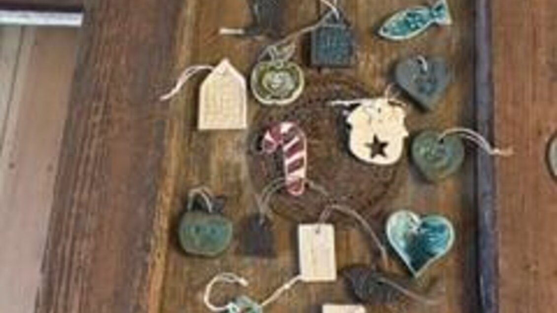 Eine Holztabelle mit verschiedenen handgemachten Anhängern. Die Anhänger haben verschiedene Formen und Farben, einschließlich Sterne, Herzen und Weihnachtsbäume. | © Keramik Werkstatt Uhring