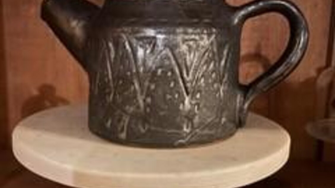 Eine dekorative Teekanne aus Keramik mit eingravierten Mustern steht auf einem runden, hellen Untersetzer. Der Untersetzer ist auf einem goldenen Sockel platziert. | © Keramik Werkstatt Uhring