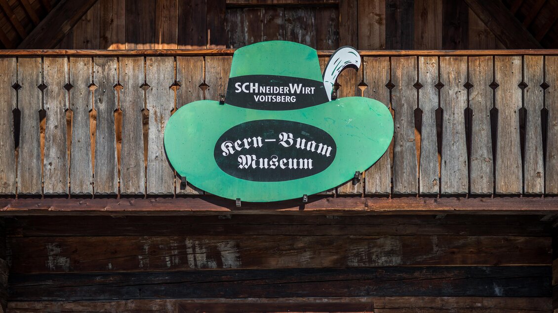Ein grünes Schild in Form eines Huts, das das "Kern-Buam Museum" anzeigt. Die Holzverkleidung und der Balkon verleihen dem Gebäude einen rustikalen Charme. | © Lipizzanerheimat - Die Abbilderei
