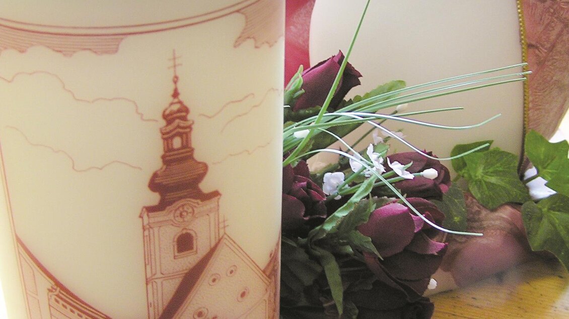 Eine dekorative Kerze mit einem Bild eines Gebäudes aus Bad Waltershausen steht auf einem Tisch. Daneben liegen Trockenblumen und eine kleinere weiße Kerze. | © Birgit Stockenreitner