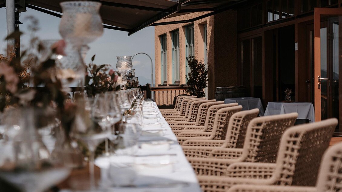Ein elegantes Restaurant mit einem langen Tisch, der für einen besonderen Anlass gedeckt ist. Im Hintergrund sind bequeme Stühle und dekorative Pflanzen zu sehen. | © Jaglhof