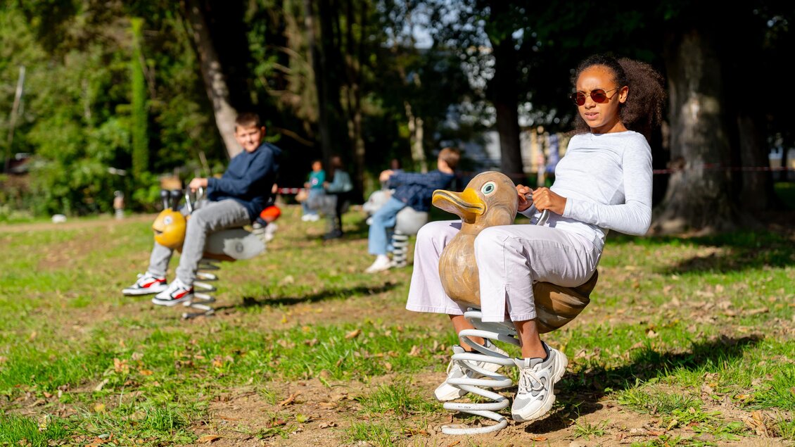 Ein Kind sitzt auf einem Schaukelspielzeug in Form einer Ente und trägt eine Sonnenbrille. Im Hintergrund sind weitere Kinder zu sehen, die ebenfalls spielen. | © © Stadtgemeinde Feldbach