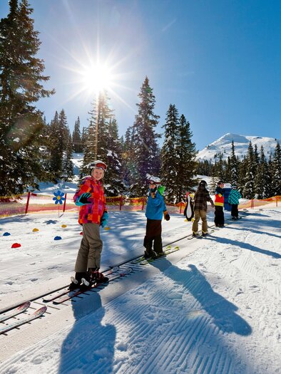 A group of skiers stands on the slope in sunny weather. Surrounded by snowy trees, they are enjoying a great ski day. | © Planneralm/Tom Lamm