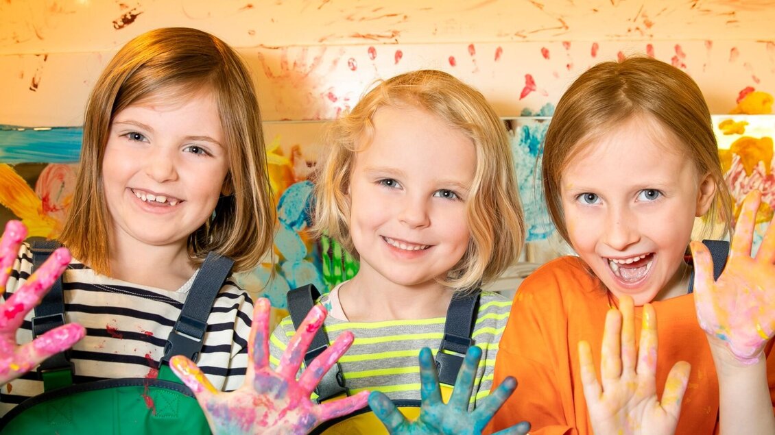 Drei lachende Kinder mit bunter Farbe an den Händen im Mitmachbereich des Kindermuseums Frida & Fred | © FRida und freD-Hannes Loske