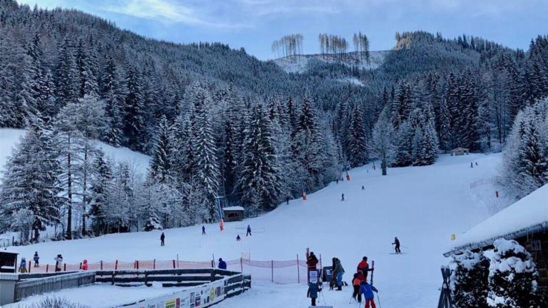 Ein schneebedecktes Skigebiet mit vielen Skifahrern. Im Hintergrund sieht man verschneite Berge und dicht bewaldete Hänge. | © Kinderschilift Pölstal