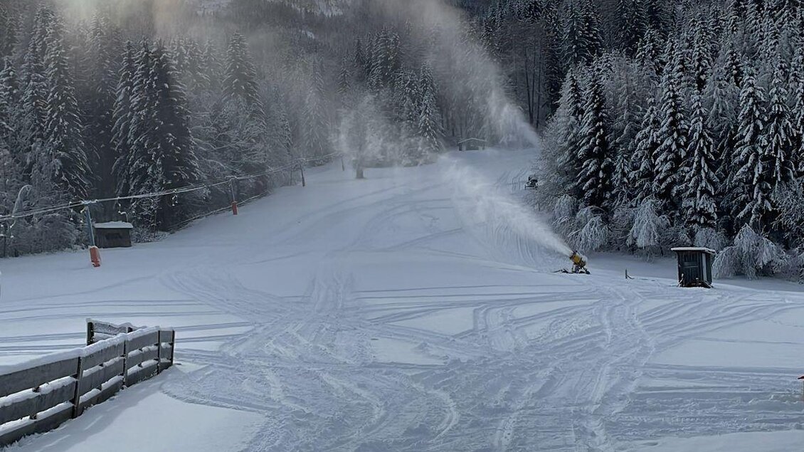 Ein verschneiter Skiweg umgeben von hohen Bäumen. Im Hintergrund sind schneebedeckte Berge und ein leicht bewölkter Himmel zu sehen. | © Kinderschilift Pölstal