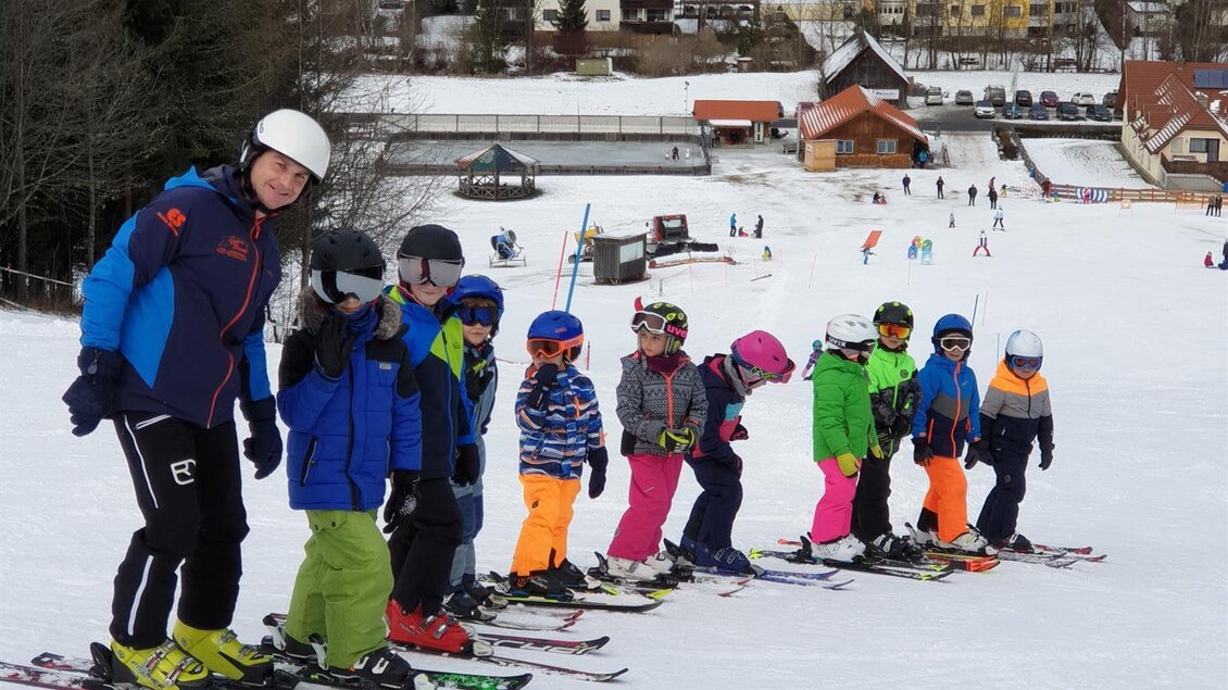 Eine Gruppe von Kindern steht in einer Reihe auf Skiern auf einer Piste. Im Hintergrund sind Häuser und Bäume sichtbar. | © Kinderschilift Pölstal