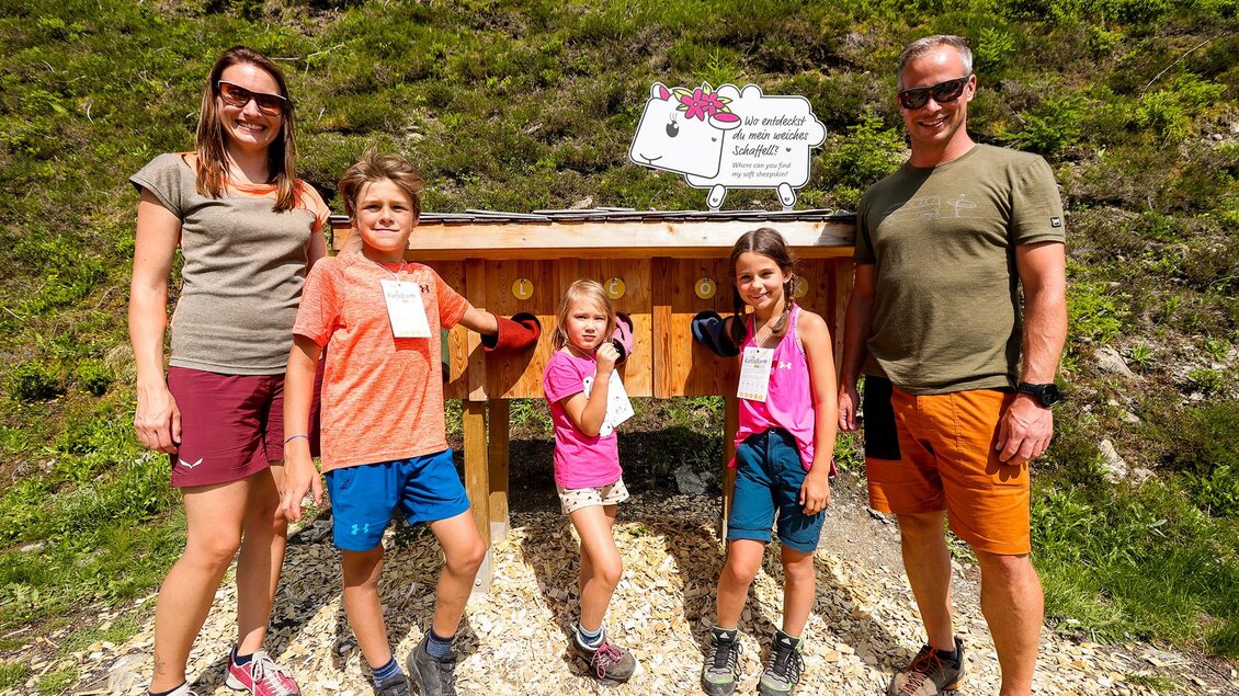 Eine Familie steht lächelnd vor einem Holzgestell im Freien. Im Hintergrund sind Bäume und eine grüne Landschaft zu sehen. | © Hauser Kaibling