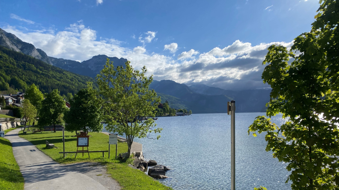 Ein schöner See umgeben von Bergen und Bäumen. Der Himmel ist teilweise bewölkt und das Wasser glitzert in der Sonne. | © Bettina Scheck