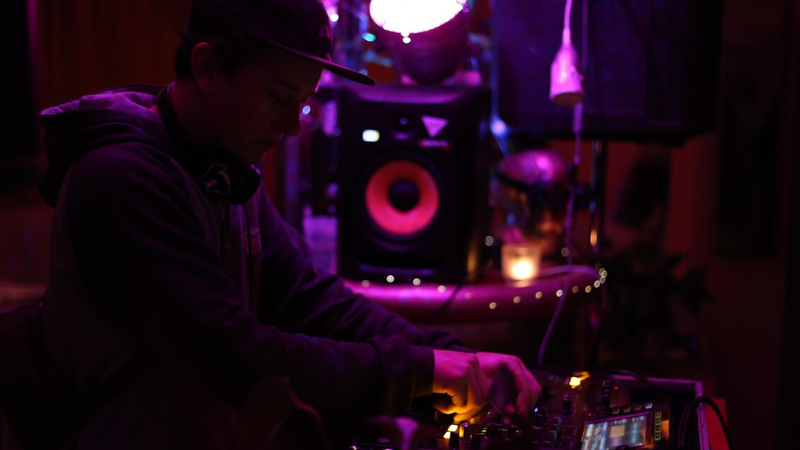 Ein DJ legt in einem dunklen Raum auf, umgeben von buntem Licht. Im Hintergrund sind Lautsprecher und eine entspannte Atmosphäre zu sehen. | © Kino Gröbming
