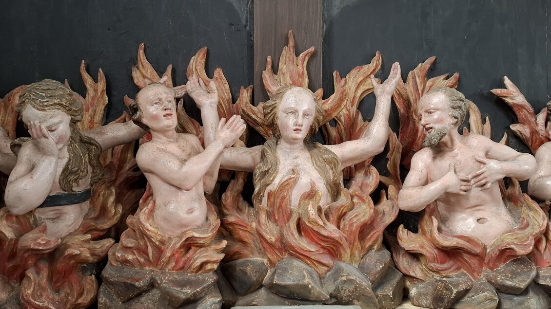 Eine Gruppe von skulpturalen Figuren steht in Flammen. Die Figuren zeigen verschiedene Emotionen und stehen auf einem steinigen Grund. | © Beate Koller