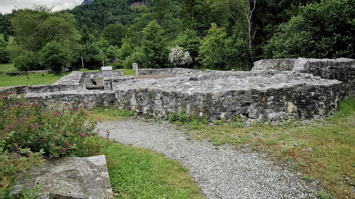 Ruinen einer alten Mauer umgeben von grüner Landschaft und Bäumen. Im Hintergrund sind Berge unter einem bewölkten Himmel zu sehen. | © Landentwicklung Steiermark