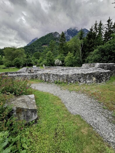 Ruinen einer alten Mauer umgeben von grüner Landschaft und Bäumen. Im Hintergrund sind Berge unter einem bewölkten Himmel zu sehen. | © Landentwicklung Steiermark