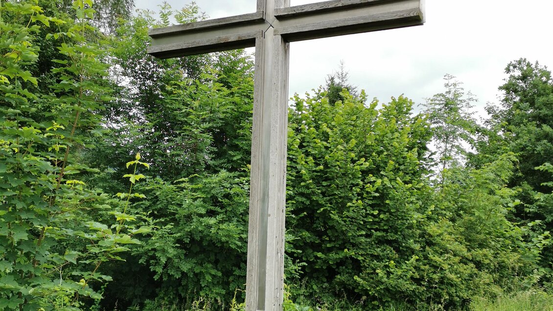 Ein großes Holz-Kreuz steht inmitten von dichtem Grün. Der Himmel ist bewölkt und es sieht nach Regen aus. | © Landentwicklung Steiermark