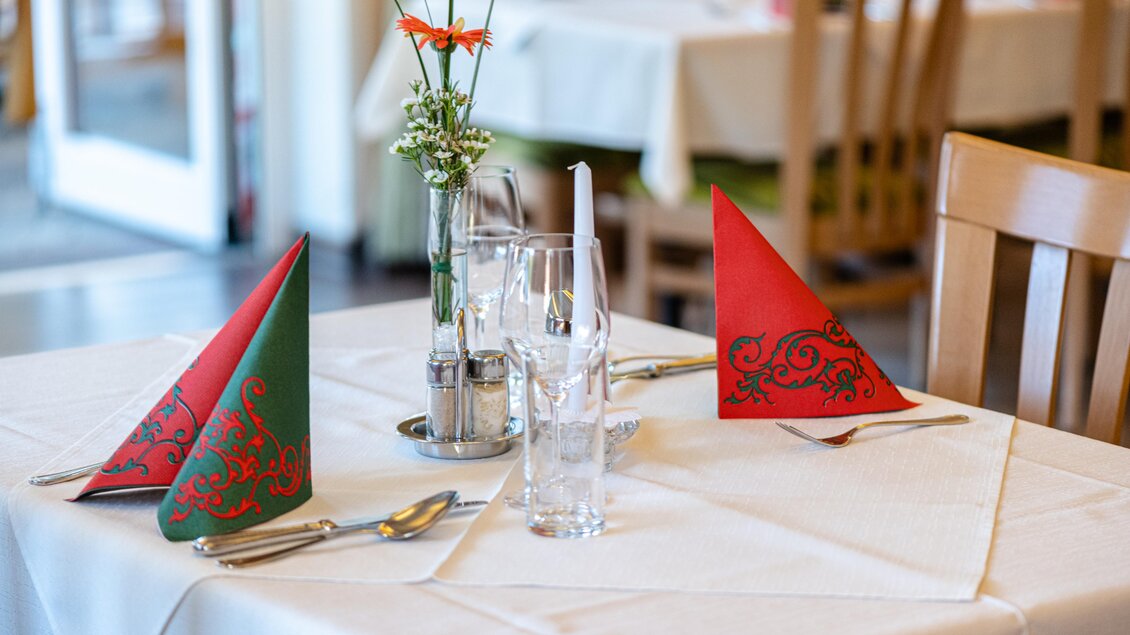 Ein schön gedeckter Tisch mit roten und grünen Servietten. Im Hintergrund sind weitere Tische und ein Blumenstrauß zu sehen. | © Martina Siebenhandl