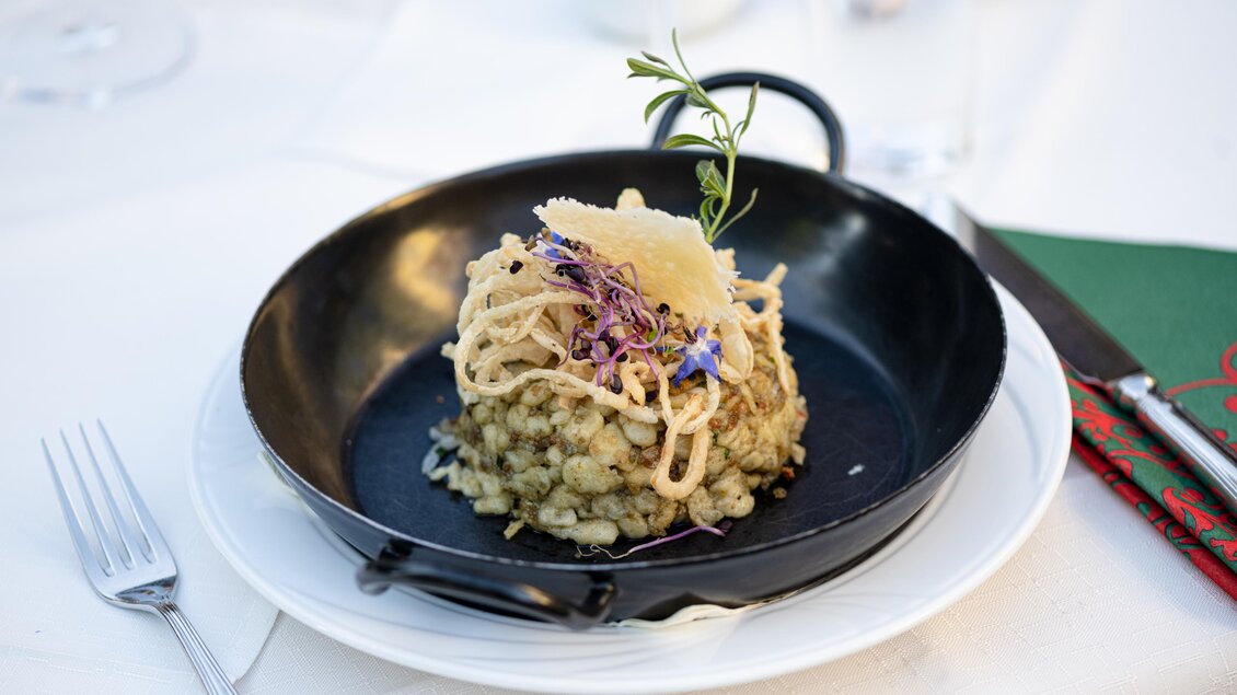 Ein elegantes Gericht auf einem schwarzen Teller. Es besteht aus einer Risotto-ähnlichen Basis mit dekorativen Zutaten und Kräutern. | © Martina Siebenhandl