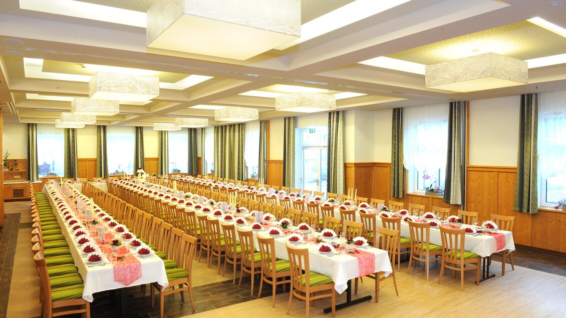 Ein festlich dekorierter Saal mit langen Tischen und Stühlen. Die Tische sind mit weißen Tischdecken und roten Akzenten eingedeckt. | © Kirchenwirt Aigen