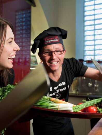 Three cheerful chefs in a kitchen are laughing and preparing fresh vegetables. There is a relaxed and inviting atmosphere. | © Kitchen12 - Christian Jungwirth