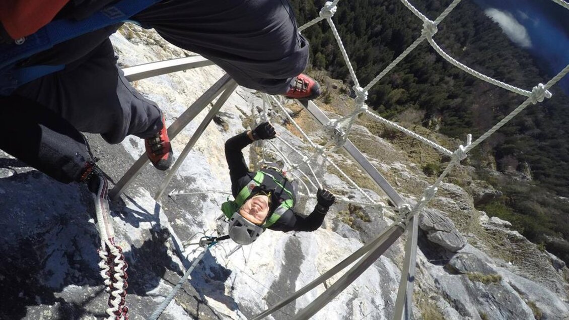 Ein Kletterer schwingt an einem Sicherungsnetz in den Bergen. Im Hintergrund sind Wälder und eine majestätische Landschaft zu sehen. | © Martin Hörzer