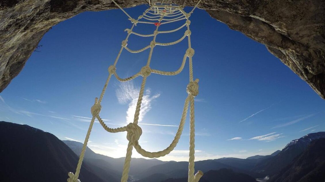 Ein Seilnetz hängt an einer Felswand, mit Blick auf eine beeindruckende Berglandschaft. Der Himmel ist klar und blau, was die Szenerie dramatisch ergänzt. | © Martin Hörzer