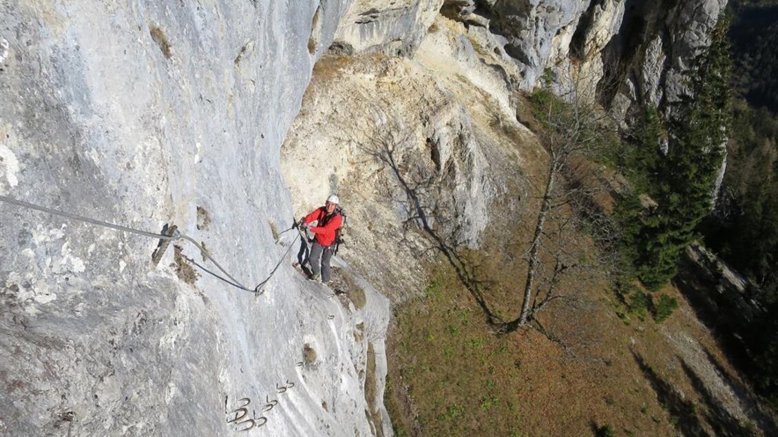 Ein Kletterer in rot steht an einer steilen Felswand. Im Hintergrund sind Bäume und felsige Landschaften zu sehen. | © Andreas Jentzsch
