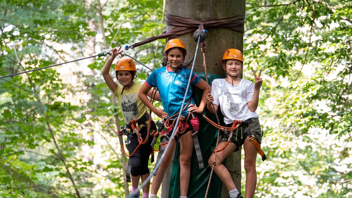 Drei Kinder stehen an einem Baum, während sie für Kletteraktivitäten gesichert sind. Sie tragen Helme und sehen glücklich und abenteuerlustig aus. | © WAP