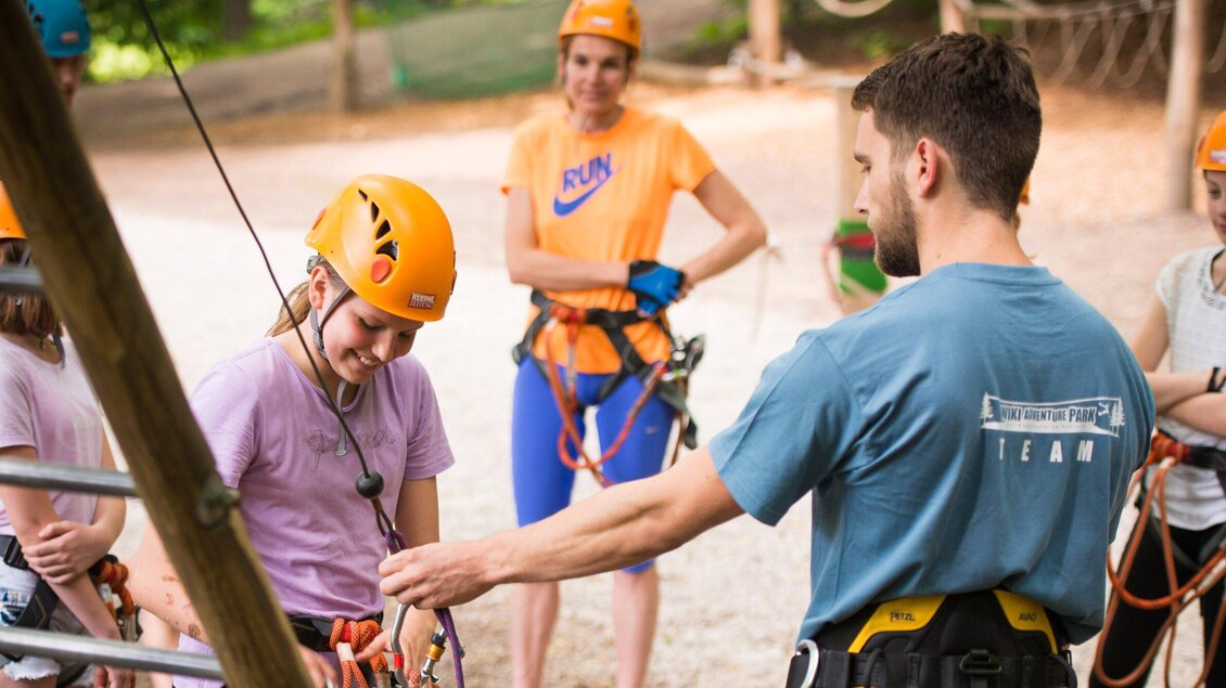 Eine Gruppe von Personen bereitet sich auf ein Kletterabenteuer vor. Sie tragen Helme und Sicherheitsausrüstung, während ein Trainer ihnen Anweisungen gibt. | © WAP