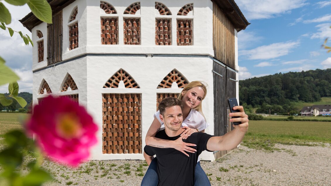 Ein Paar macht ein Selfie vor einem historischen Bauwerk. Im Vordergrund ist eine Blume zu sehen. | © TV Region Graz - Harry Schiffer