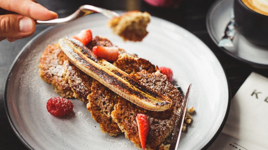 Ein Teller mit köstlichen Pfannkuchen, garniert mit einer gegrillten Banane und frischen Beeren. Dazu gibt es eine Tasse Kaffee. | © Klyo - Aaron Jiang