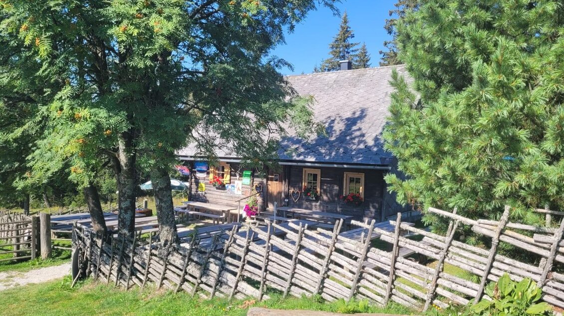 <p>Almhütte mit Holzzaun, Sitzbänken und Bergen im Hintergrund bei Hirschegg‑Pack. </p> | © Mathias Renhart