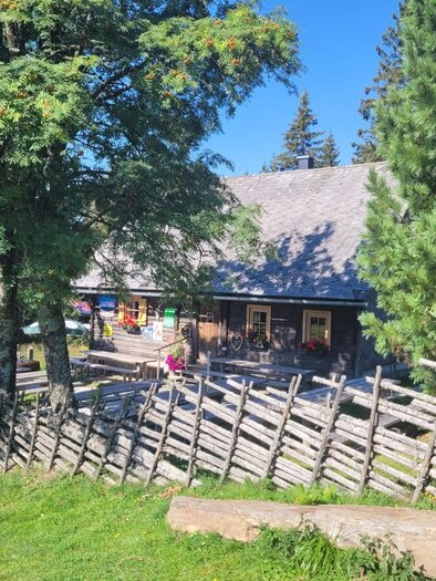<p>Almhütte mit Holzzaun, Sitzbänken und Bergen im Hintergrund bei Hirschegg‑Pack. </p> | © Mathias Renhart